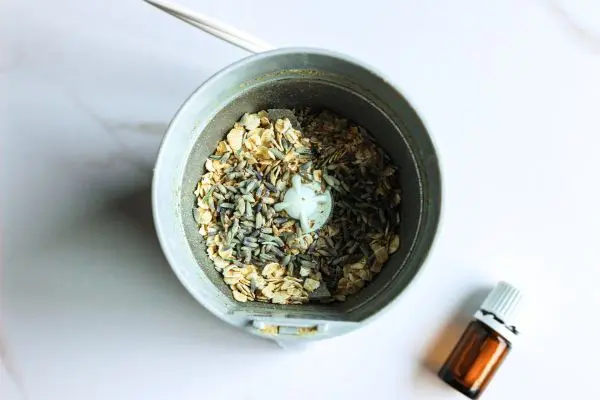 Lavender Tallow Oatmeal Face Scrub Recipe 15 a coffee grinder containing oats and lavender for making a lavender tallow face scrub. bottle of essential oil next to it.
