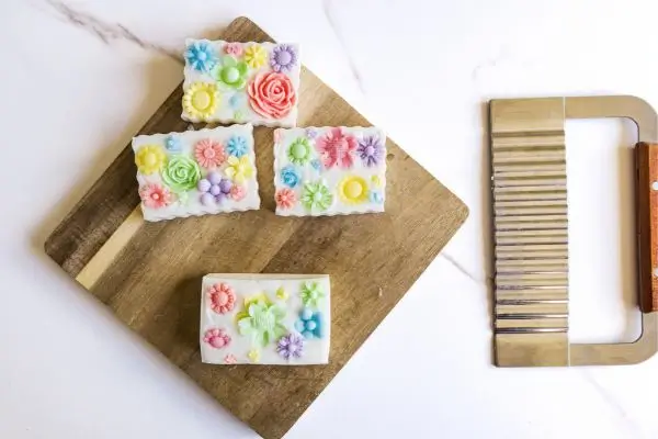 DIY Floral Soap Bars - an impressive handmade gift 36 wooden cutting board with homemade floral soaps on it and a wavy soap cutter tool on the side