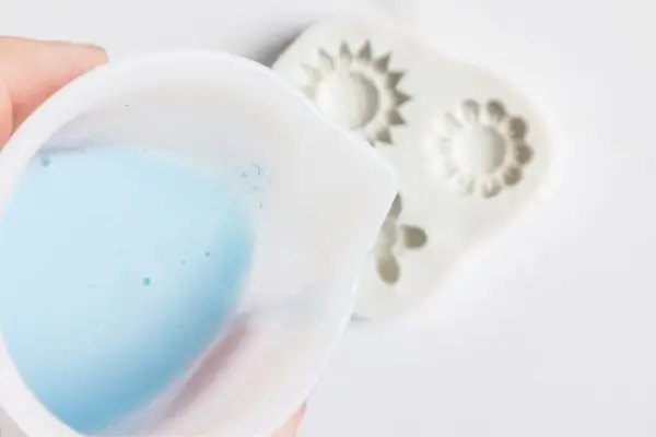 DIY Floral Soap Bars - an impressive handmade gift 27 a cup of blue soap base being poured into a small flower soap mold.