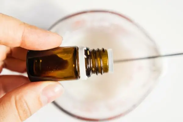 DIY Floral Soap Bars - an impressive handmade gift 31 a glass measuring cup filled with melted soap base, and a woman's hand adding drops of essential oil from a bottle.