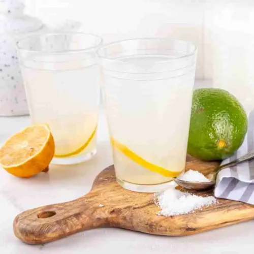 Homemade Electrolyte Drink Powder (Natural DIY Recipe) 10 a glass of homemade electrolyte drink on a wood cutting board with a spoonful of the powder, lemon and lime